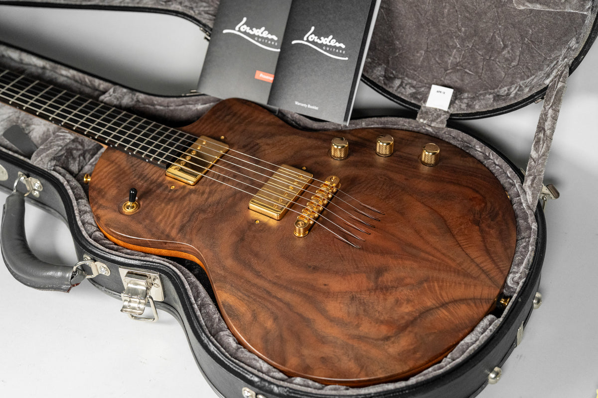 Walnut-topped electric guitar with gold hardware, including two humbuckers and four control knobs, resting in a black hard case.