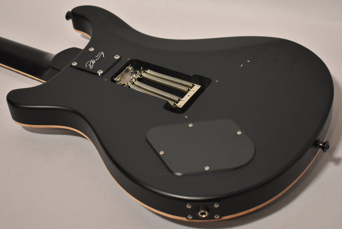 The guitar's matte black back shows a tremolo spring cavity, control plate, output jack, and strap button, with minor finish wear.