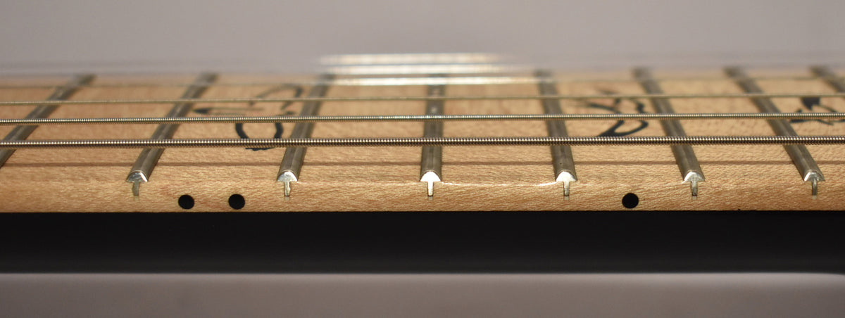 Close-up of the light-colored maple fretboard and frets, with black side dots and dark fretboard inlay visible.
