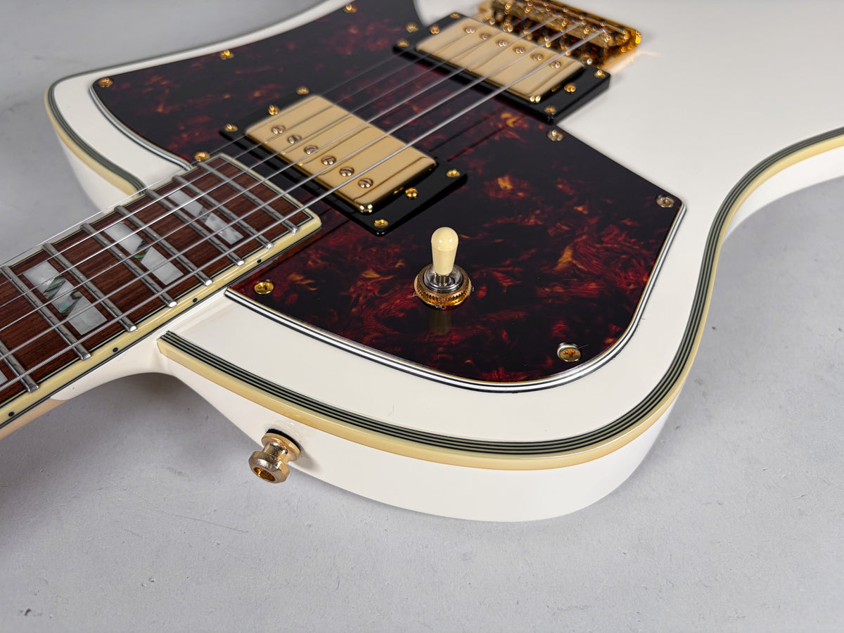 Close-up of the white guitar body, showing the tortoise shell pickguard, gold humbuckers, cream switch tip, and output jack.