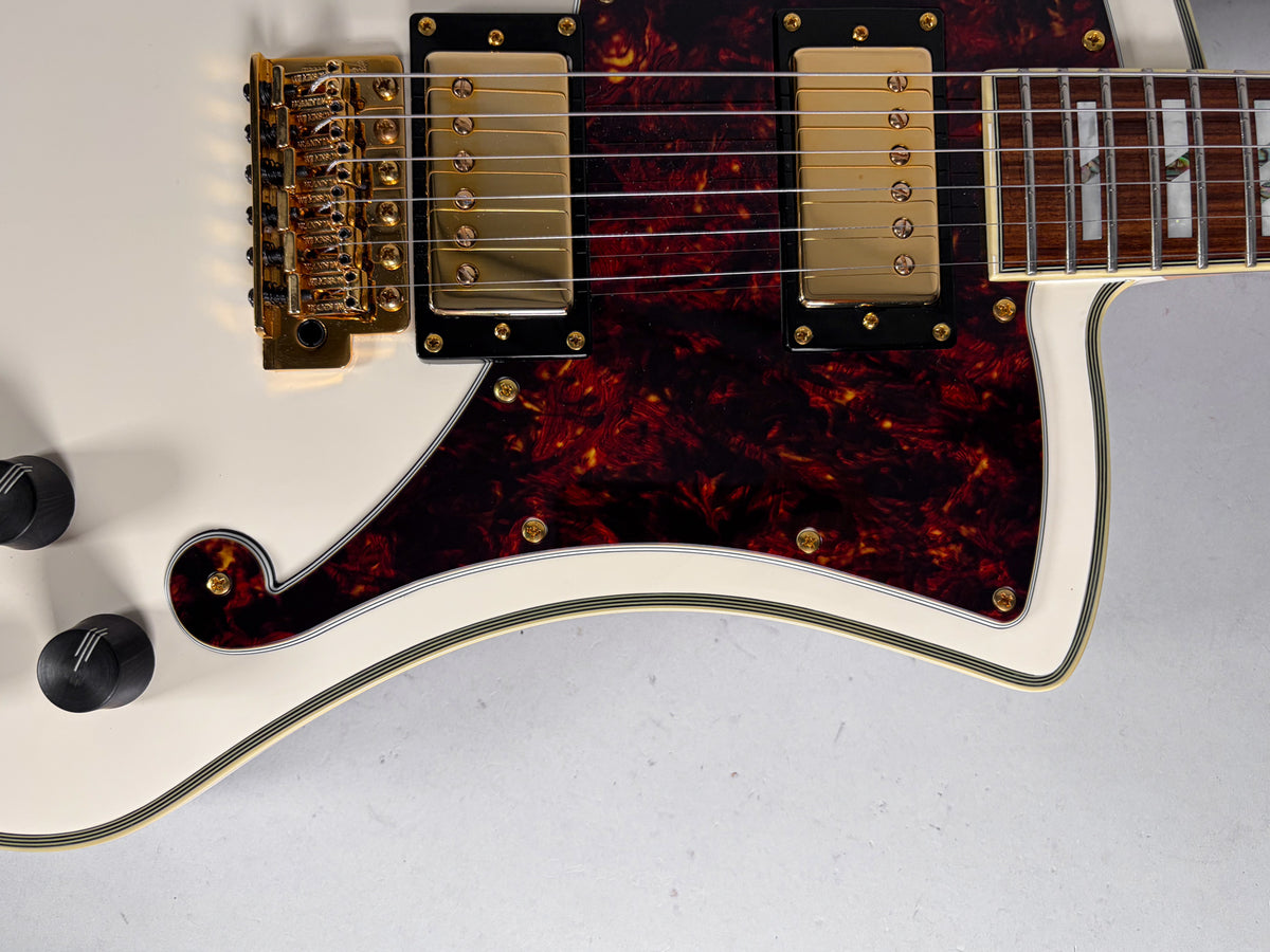 Close-up of the white guitar body, showing two gold humbuckers on a tortoiseshell pickguard, gold tremolo, and black control knobs.