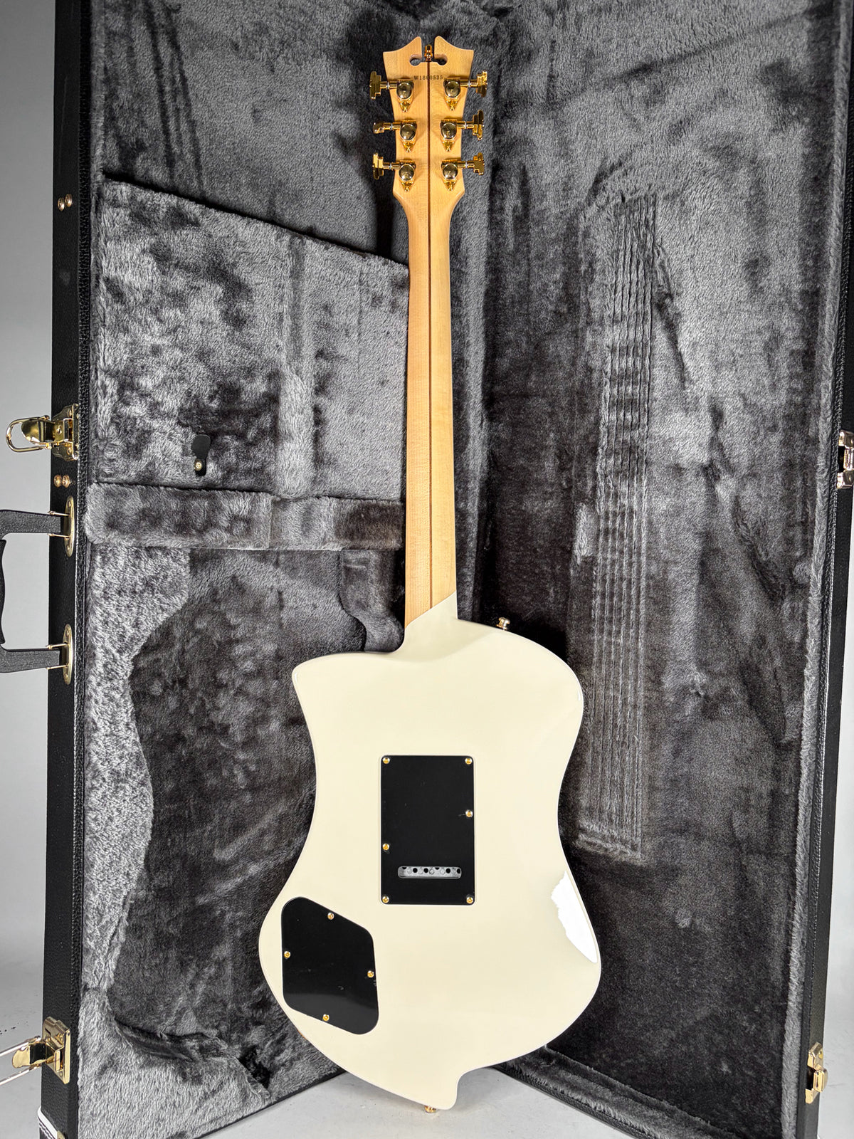 The guitar's back is visible, showing a white finish, two black control plates, and a maple neck with gold tuners.