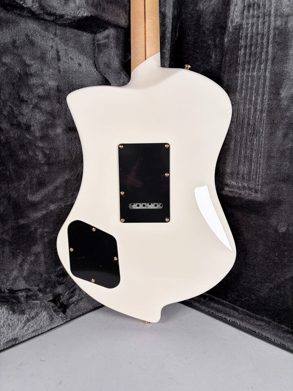 The back of a white electric guitar with a natural wood neck, two black control plates, and a small scratch on the upper bout.