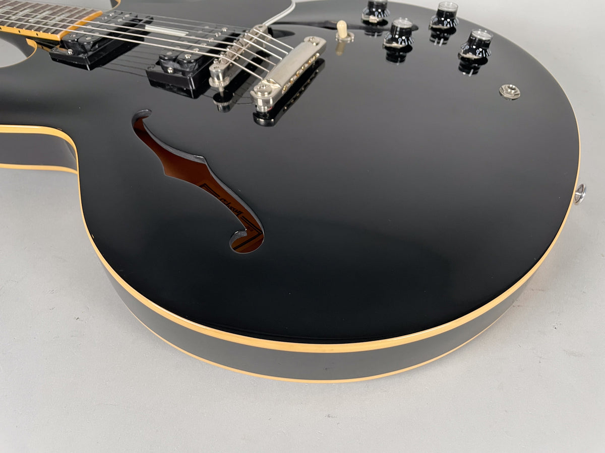 Close-up of the glossy black guitar body, showing the f-hole, two humbuckers, tune-o-matic bridge, and four black control knobs.