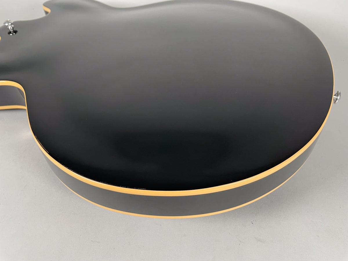 The back of the black semi-hollow guitar, showing its matte finish and cream binding along the curved edges.