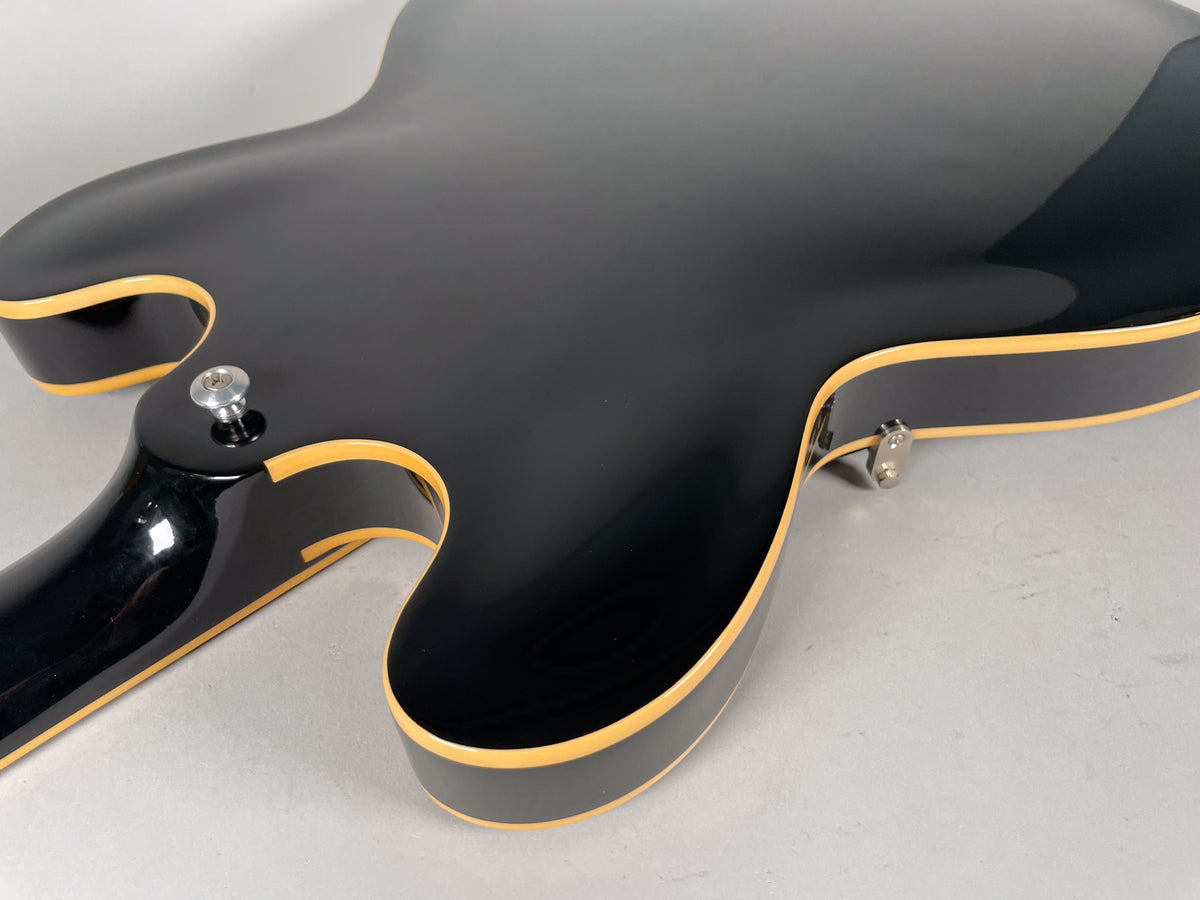 Close-up of the glossy black ES-335's lower bout and neck heel, showing cream binding and a chrome strap button.