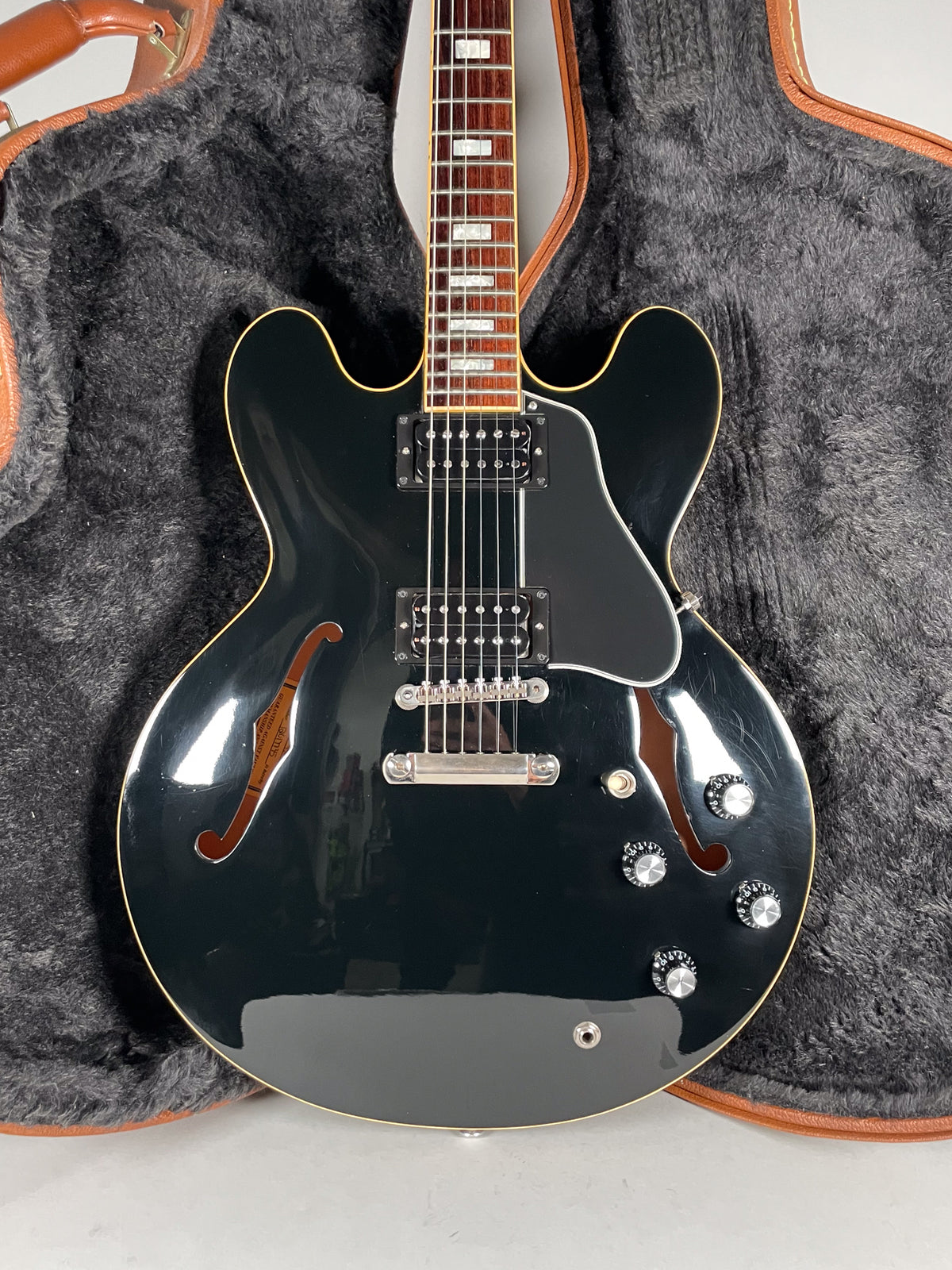 Full front view of a glossy black semi-hollowbody electric guitar with two humbuckers, a pickguard, and four control knobs.