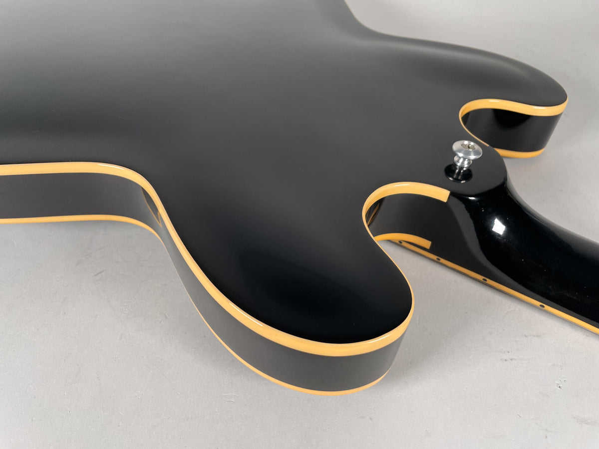 Close-up of the guitar's glossy black body and neck joint, showing the cream binding along the edges and a chrome strap button.