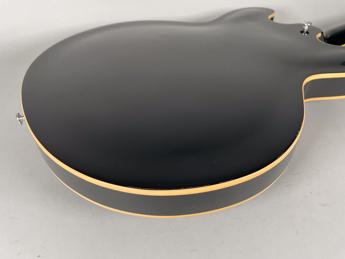 The guitar's glossy black back and side are visible, with cream binding along the edges and a chrome strap button on the lower bout.
