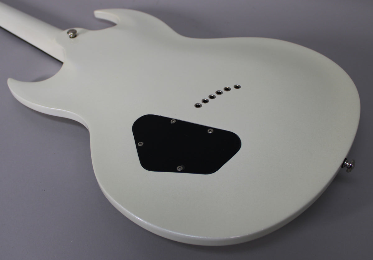 The back of a white guitar body, angled from the neck joint to the lower bout, shows a black control cavity cover and six string-through ferrules.