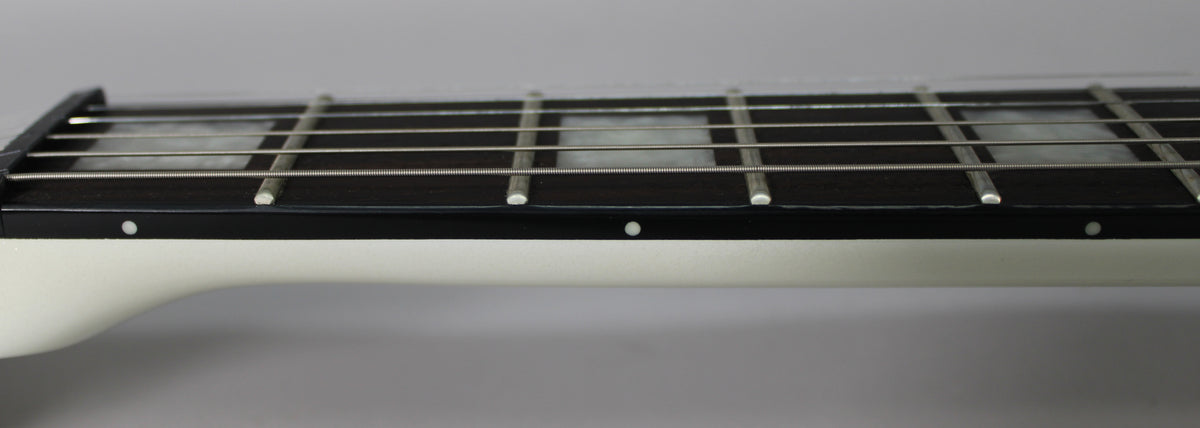 Close-up of the guitar's fretboard, showing white rectangular inlays, side dots, and a white neck against a grey background.
