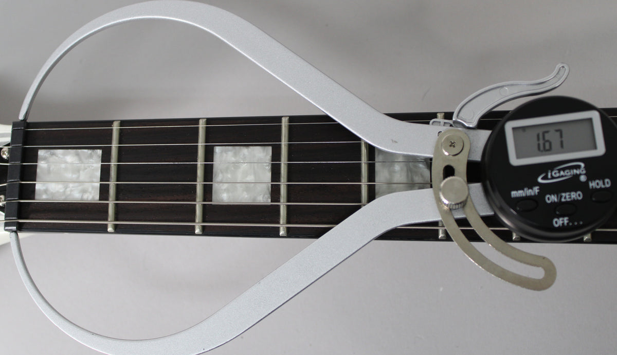 Close-up of the dark fretboard with mother-of-pearl block inlays, showing a digital caliper measuring fret height at 1.67mm.
