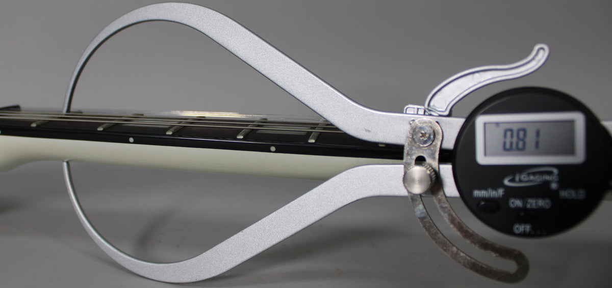 A digital caliper measures the string height at 0.81mm on the white guitar neck with a dark fretboard and dot inlays.