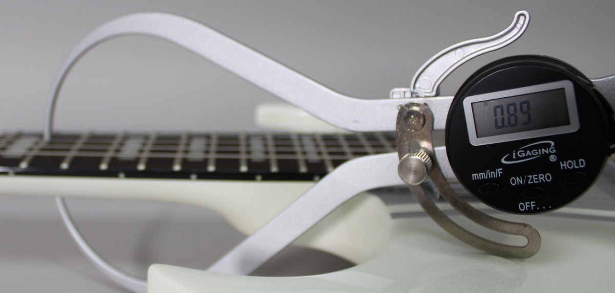 Close-up of the white guitar's fretboard and neck, with a digital caliper measuring the string height at 0.89.