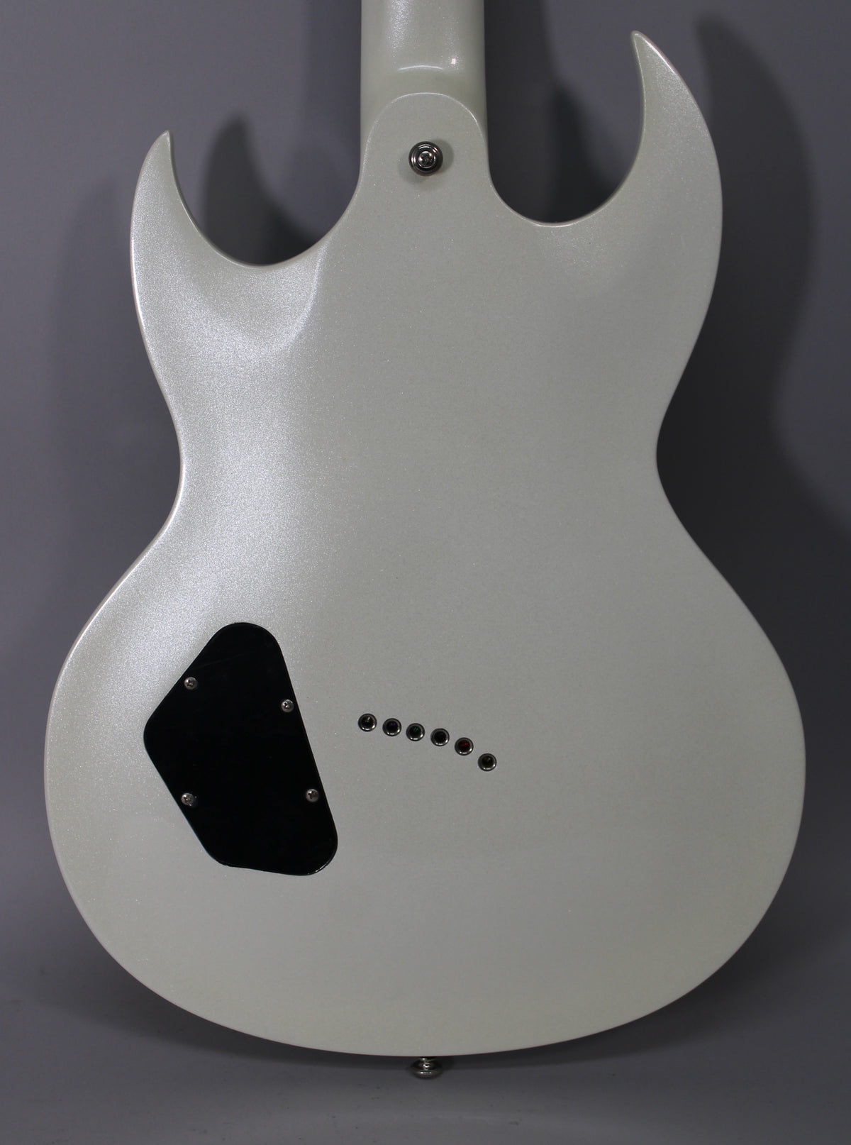 The back of a metallic white guitar with a black control cavity cover and six string-through-body ferrules.