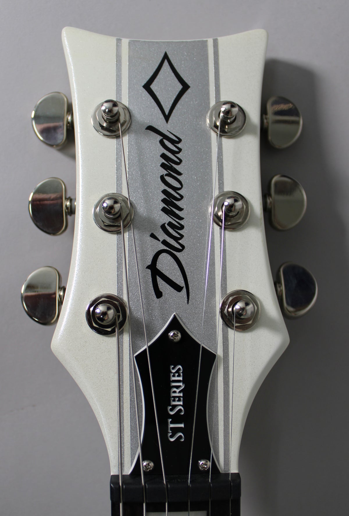 Close-up of the white sparkle headstock with a silver metallic stripe, six chrome tuners, and a black truss rod cover.