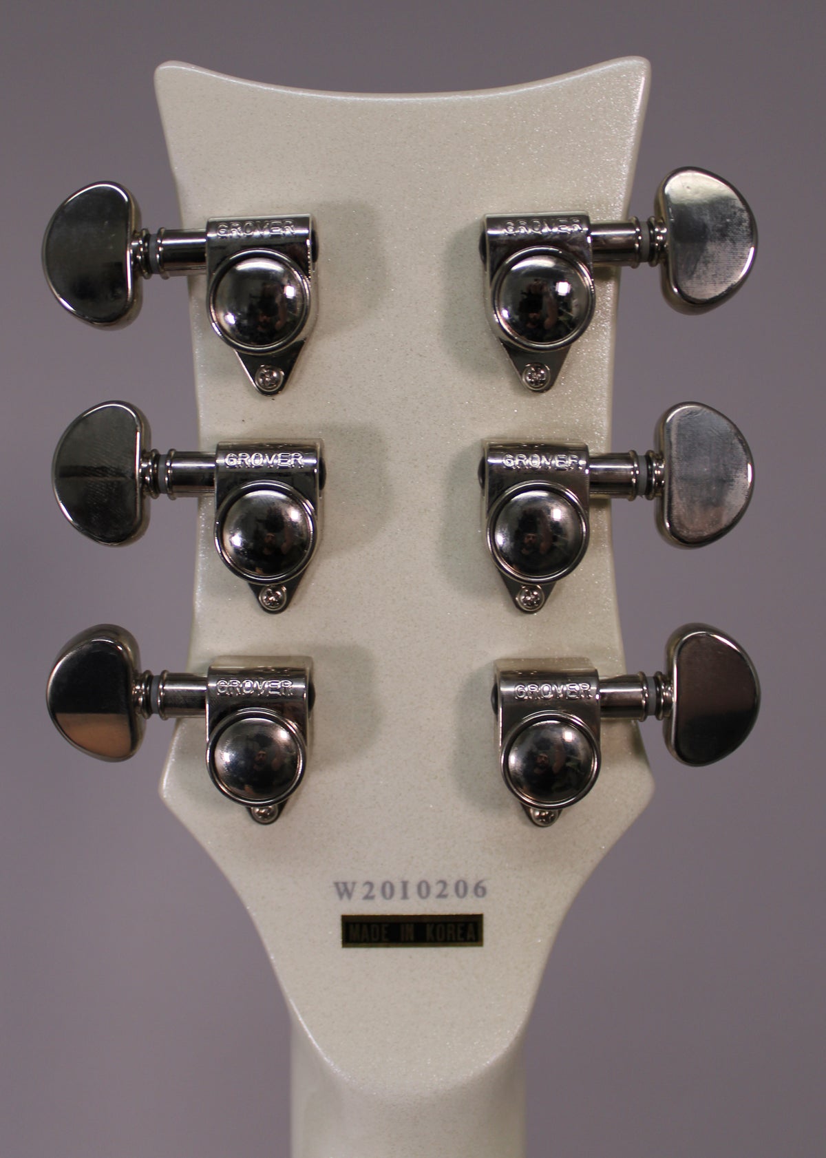 Rear view of the white sparkle headstock, showing six chrome tuners with kidney-shaped buttons, arranged 3x3.