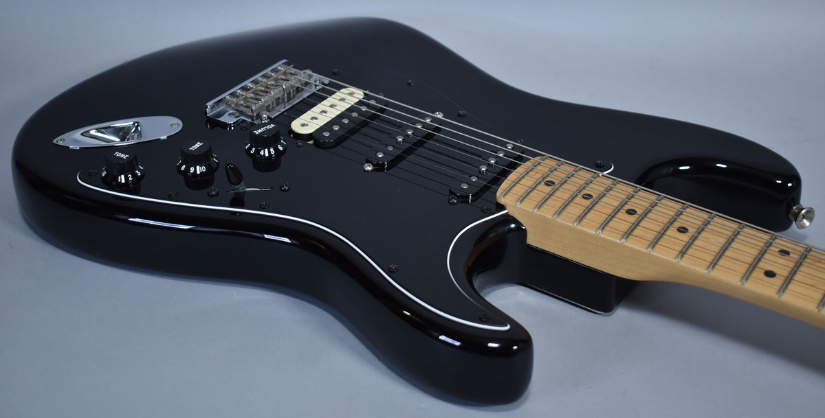 Black Stratocaster body with a glossy finish, white pickguard, chrome hardware, and a maple neck, viewed from above.