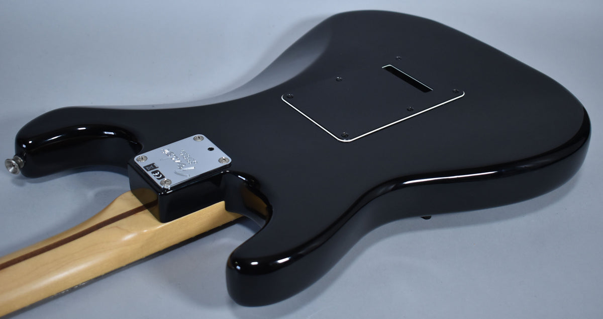 The black Stratocaster's glossy back is angled, showing the neck plate, output jack, and the tremolo cavity cover.