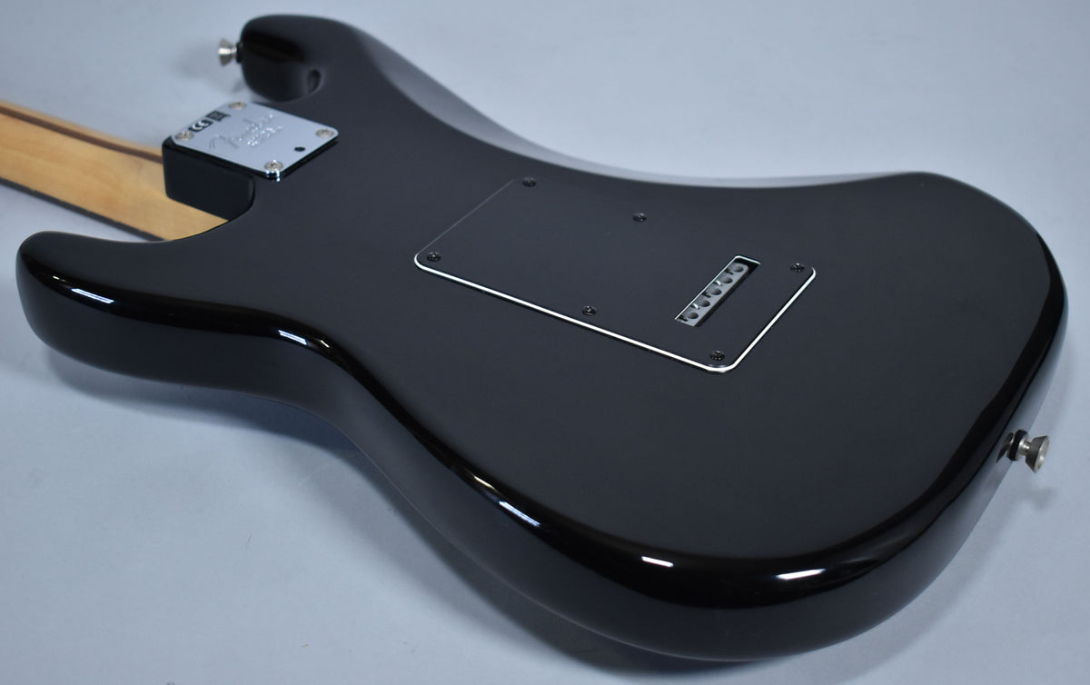The glossy black guitar body is viewed from the back, showing the neck plate, tremolo cavity cover, and strap button.