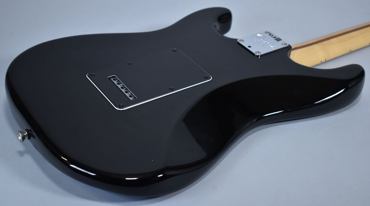 The black Stratocaster's glossy back shows a tremolo spring cover, string-through-body ferrules, and a chrome neck plate.