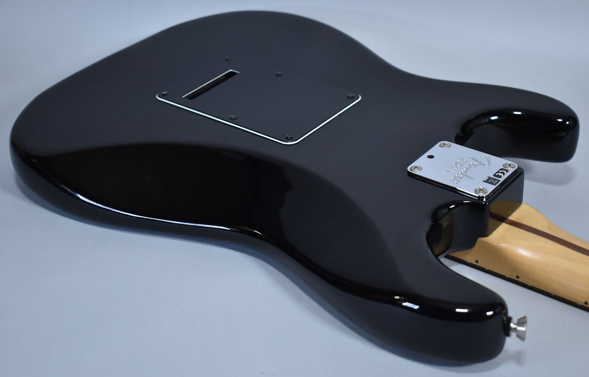 The glossy black Stratocaster body is viewed from the back, showing the tremolo cavity cover, neck plate, and strap button.