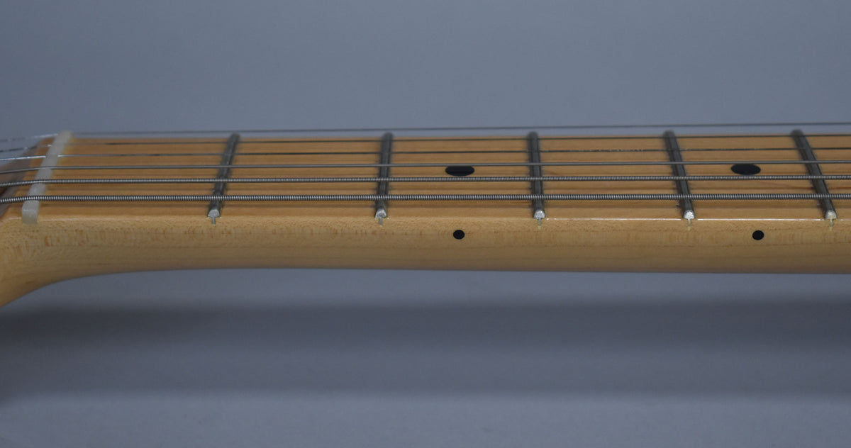 Close-up of the maple fretboard and frets, showing black dot inlays and side markers, with light wear on the fretboard edge.