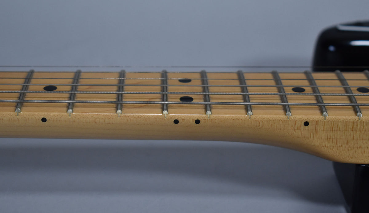 Close-up of the maple fretboard and frets, showing black dot inlays and side markers, with a hint of the black body.