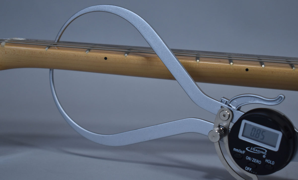 A digital caliper measures the maple neck's thickness at 0.85 inches, showing the fretboard with dot inlays and strings.