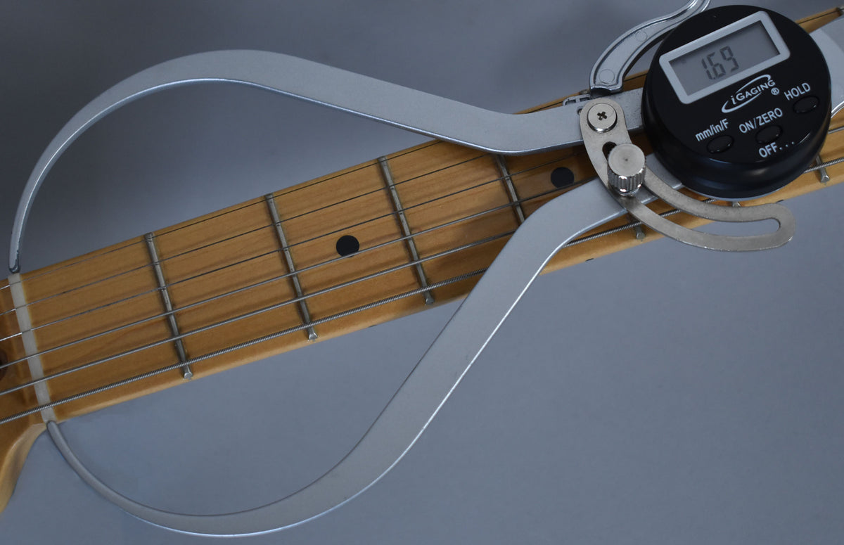 A digital caliper measures the width of the light-colored maple fretboard, showing 1.69 inches on its black display.