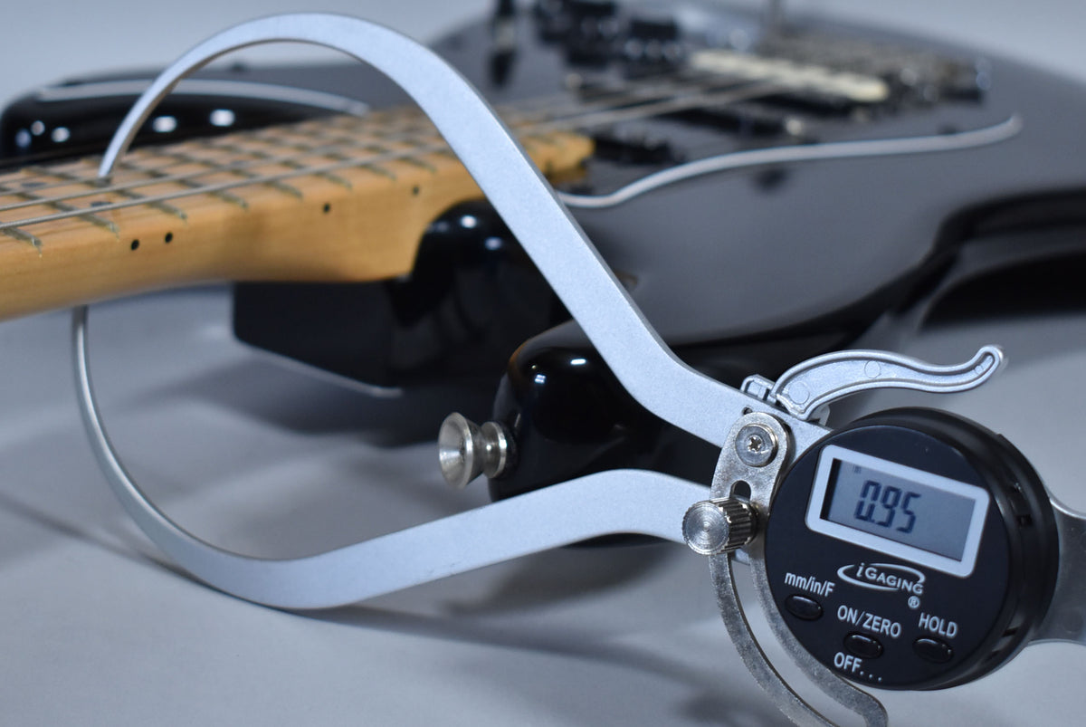 A digital caliper measures the black guitar's neck thickness at the first fret, showing a reading of 0.95.