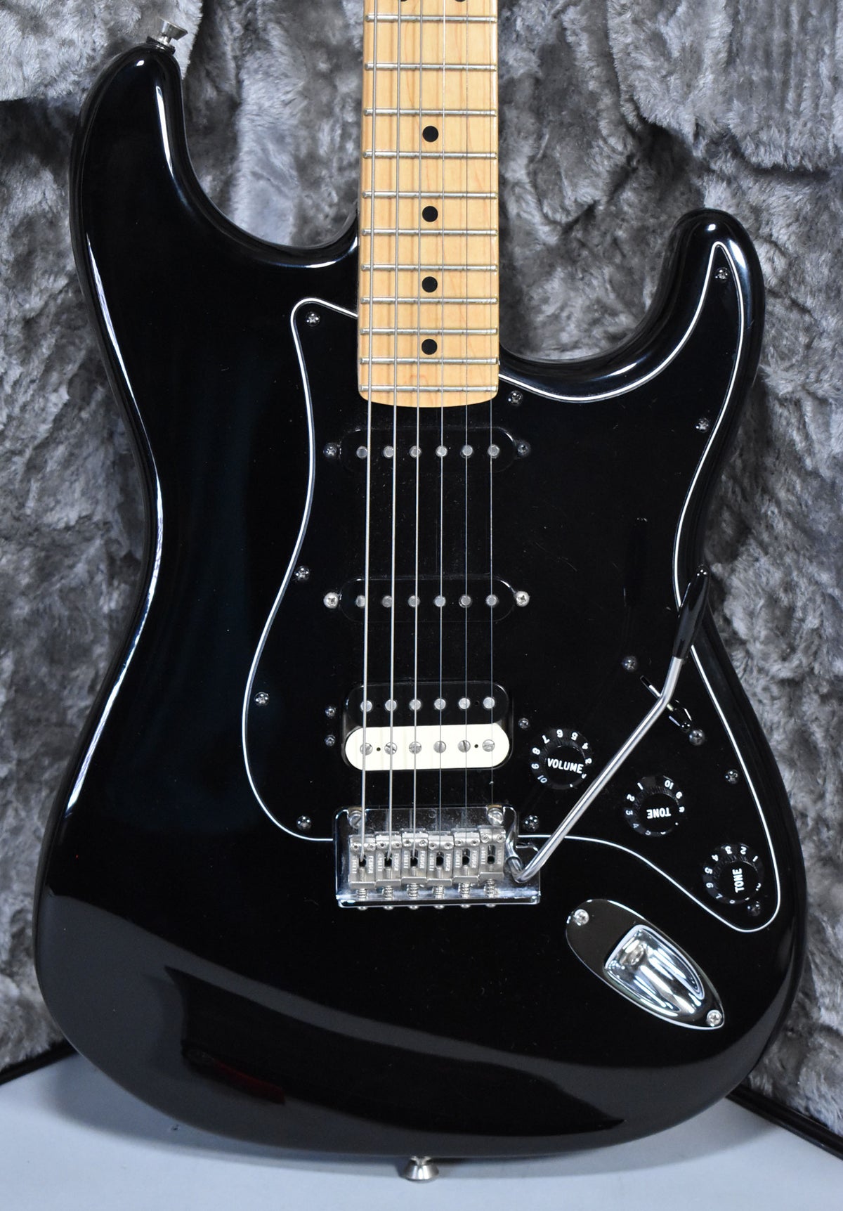 A black Stratocaster with a maple fretboard, black pickguard, two single-coil pickups, a white humbucker, and a tremolo bar.