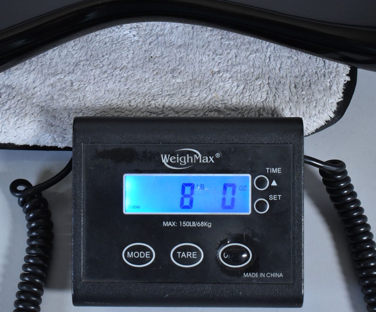 A black digital scale displays "8 LB. 0 OZ." with a black guitar body resting on a grey towel above it.