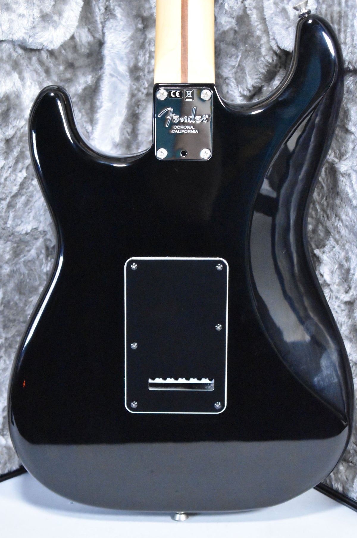 The back of a glossy black Stratocaster, showing the neck plate, light maple neck, and rectangular tremolo cover.