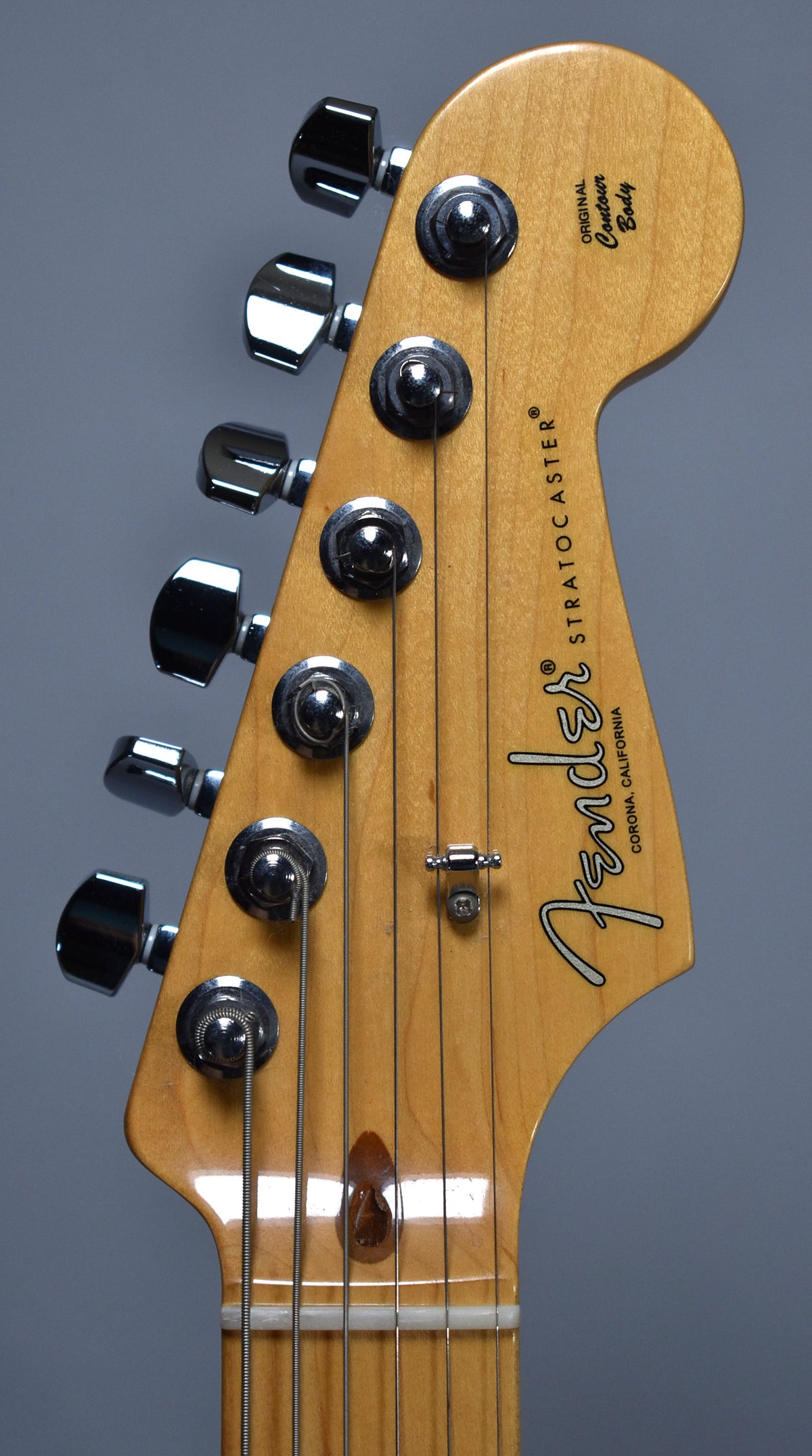 Close-up of the light brown headstock with six chrome tuners, a string tree, and a dark brown string retainer.