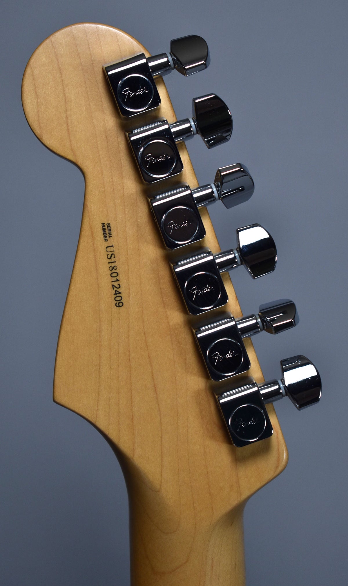 Rear view of the light-colored maple headstock and neck, showing six chrome tuning machines and a serial number on the headstock.