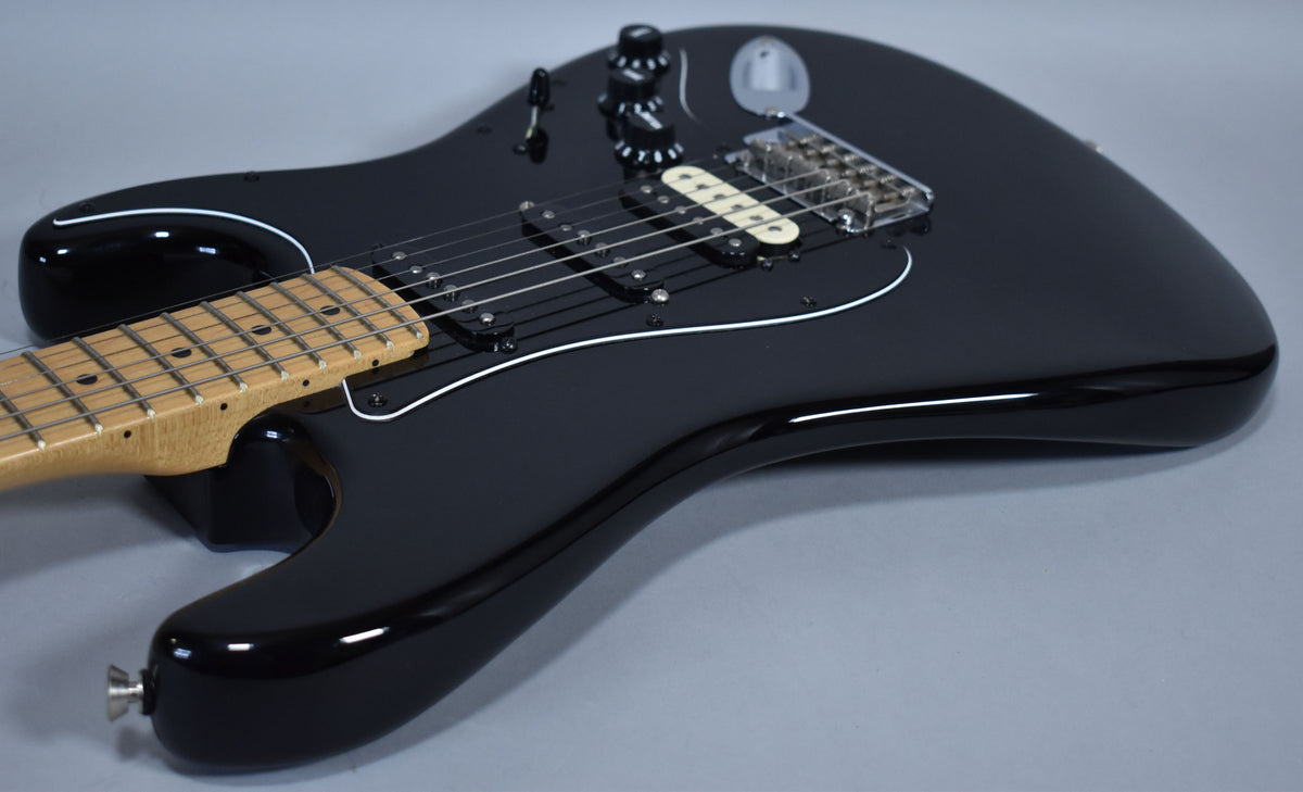 The black Stratocaster's body is angled from the lower left, showing its maple neck, black pickguard, and cream humbucker.