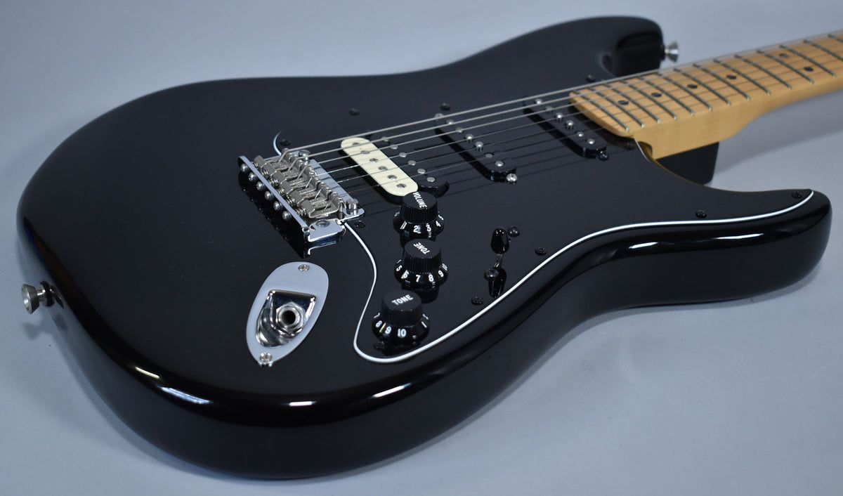 A glossy black electric guitar, angled to show the body, pickguard, controls, and part of the maple neck.