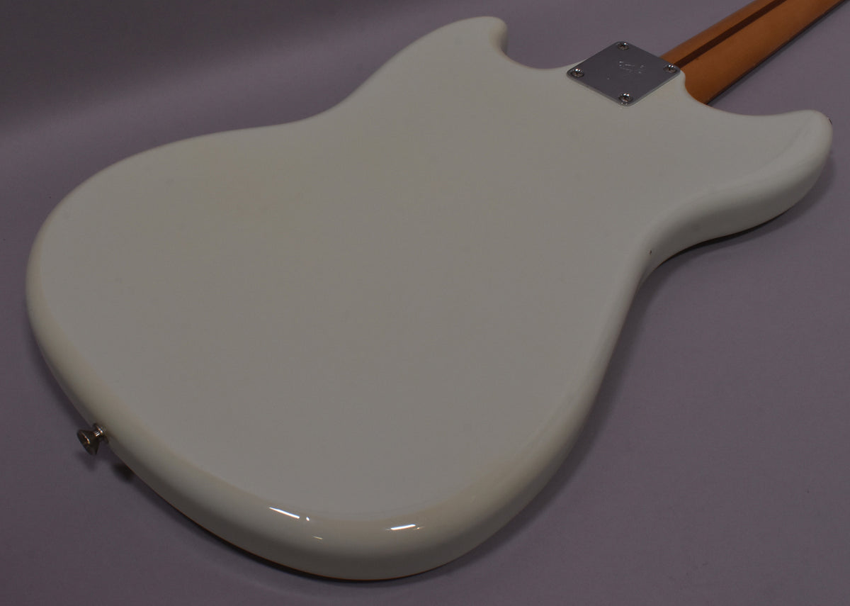 Back of a white bass guitar with a chrome neck plate and a light wood neck.