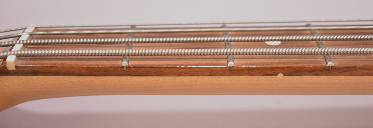Close-up of the bass neck and fretboard, showing four strings, white fret markers, and a light-colored nut.