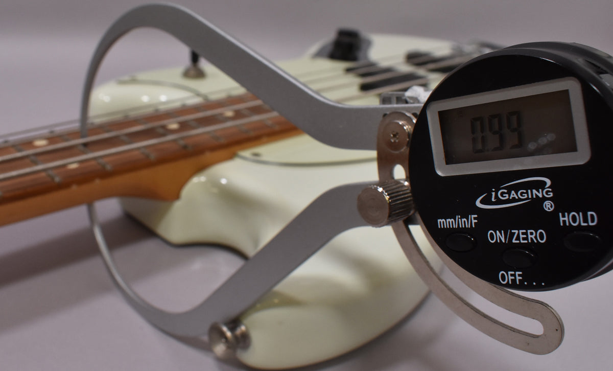 A digital caliper measuring the neck of a white bass guitar, displaying "0.99".