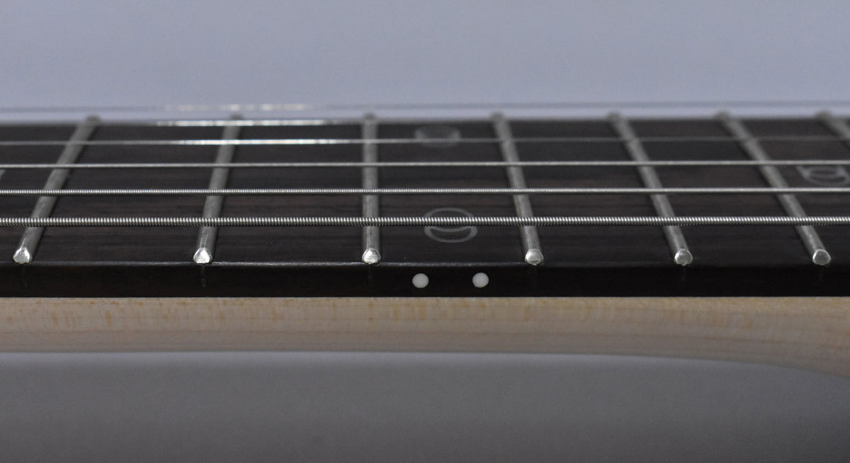Close-up of the dark fretboard and light maple neck, showing two white side dots and subtle circular fret markers.