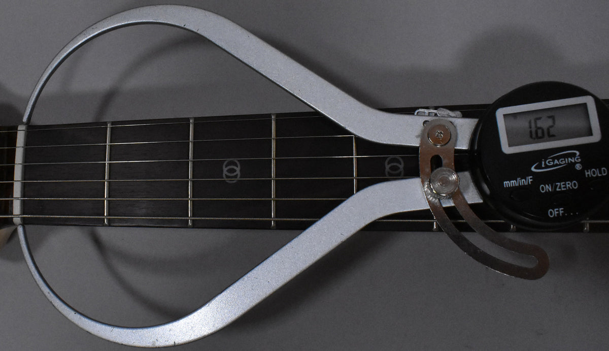 A digital string action gauge measures 1.62mm on the dark fretboard with circular inlays, showing frets 1-5.