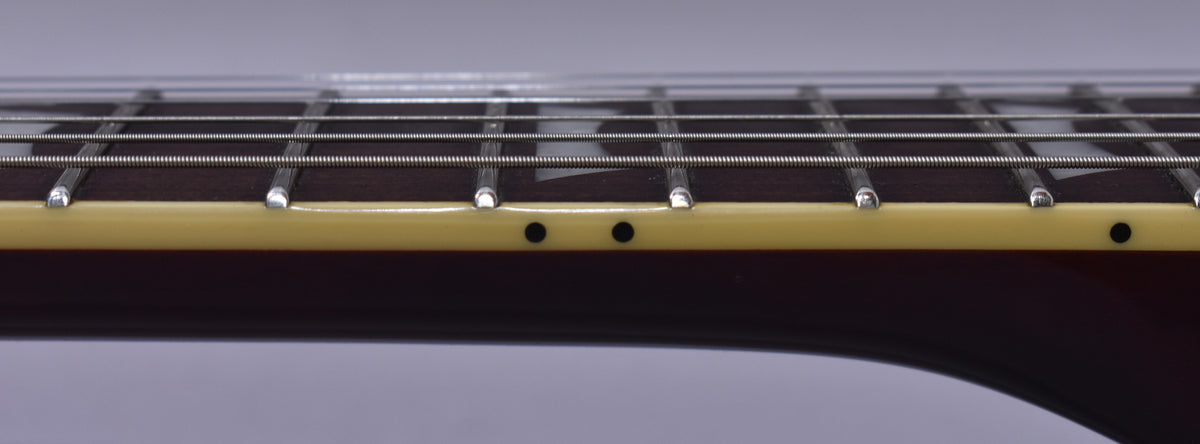 Close-up of the guitar's dark fretboard and frets, with cream binding and black side dot markers, viewed from the bass side.