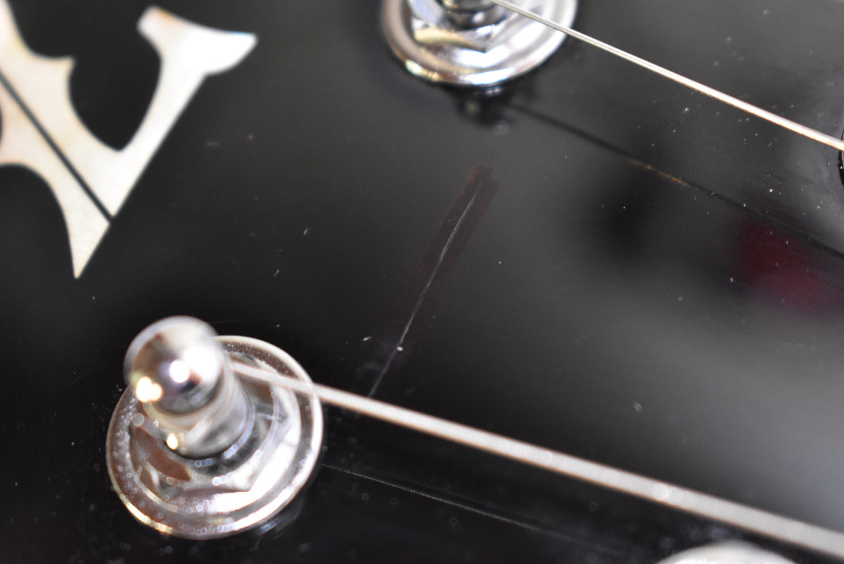 Close-up of the glossy black headstock with chrome tuners and a visible scratch between two tuning pegs.