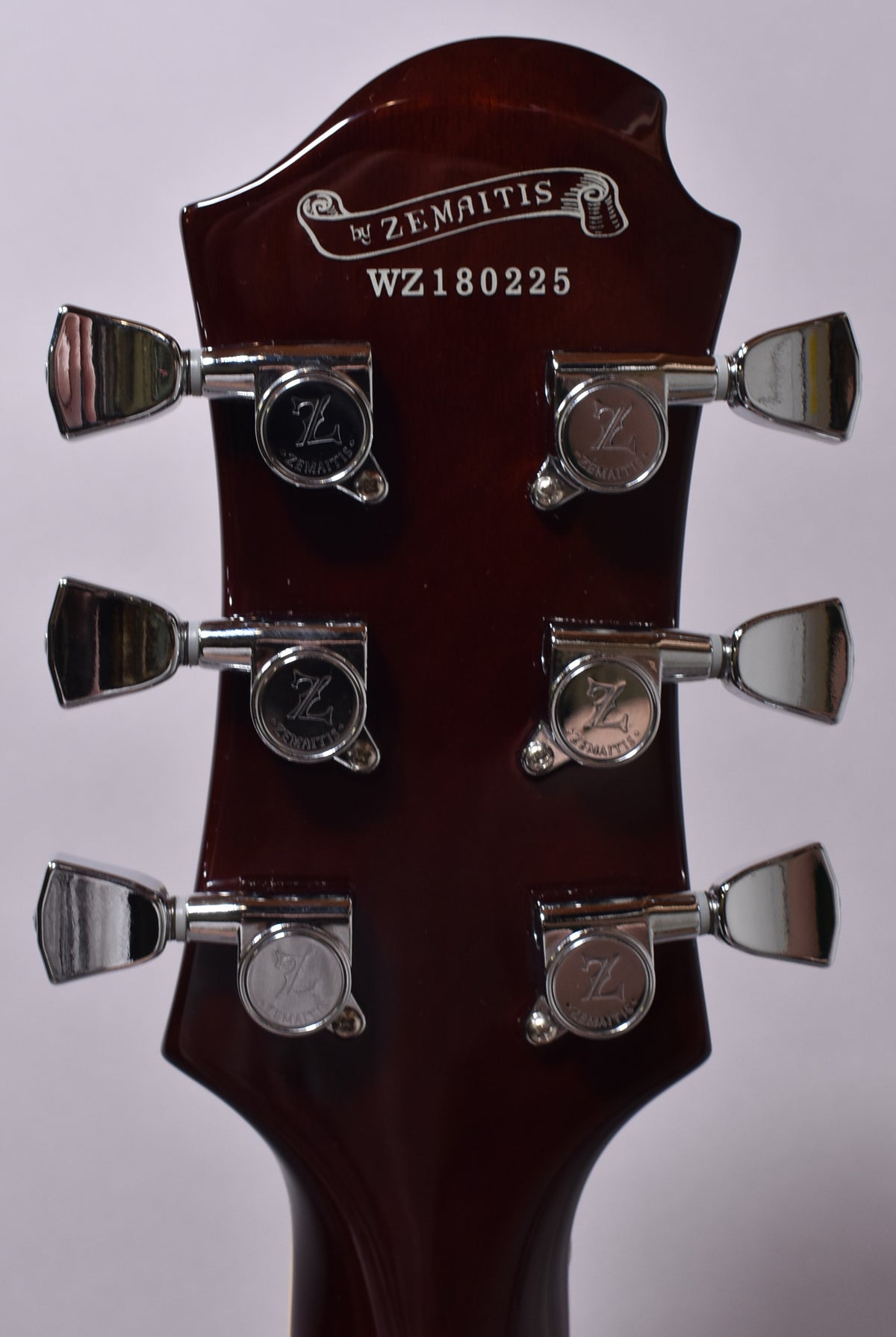 The back of a dark brown headstock with a glossy finish, featuring six chrome tuners arranged 3x3.