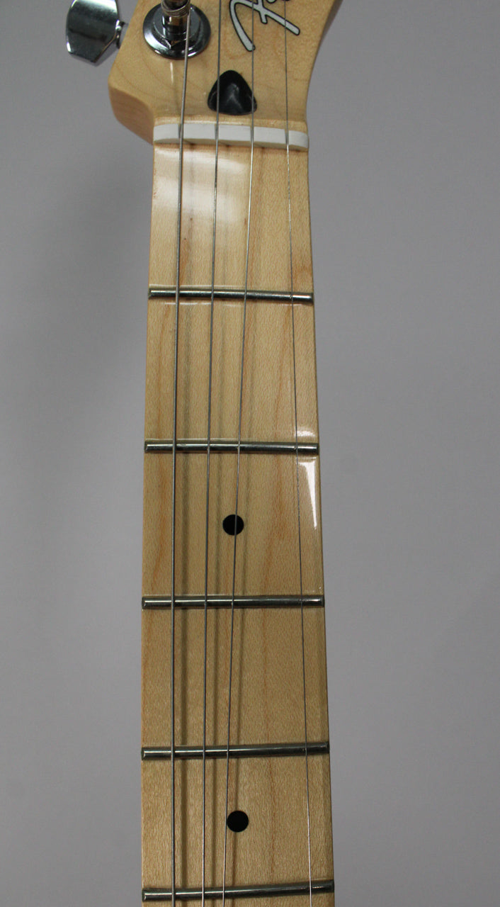Close-up of the light wood fretboard and headstock, showing four strings, chrome tuners, and black dot inlays.