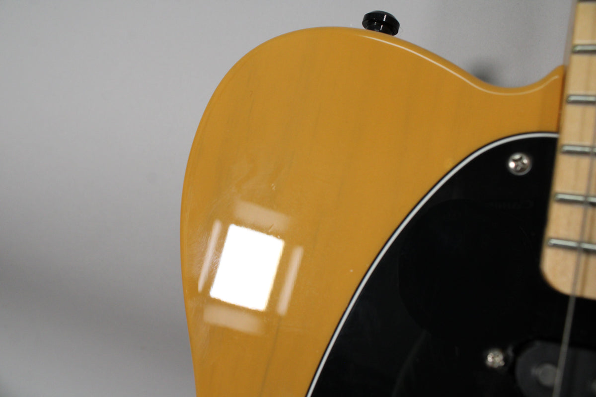 Close-up of the guitar's upper bout in glossy butterscotch blonde, showing light surface scratches and a black pickguard with white trim.