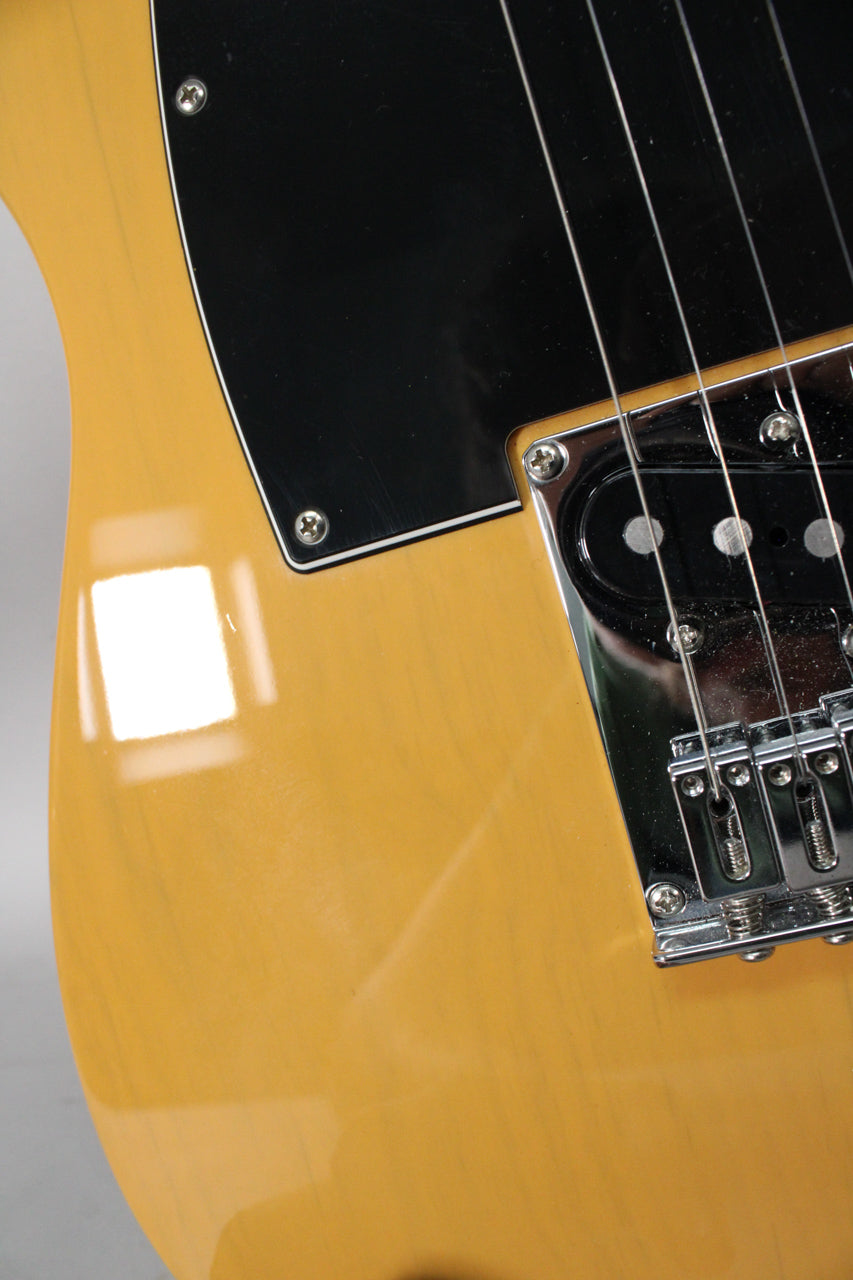 Close-up of the glossy butterscotch body and black pickguard, showing the chrome bridge with four strings and a single coil pickup.