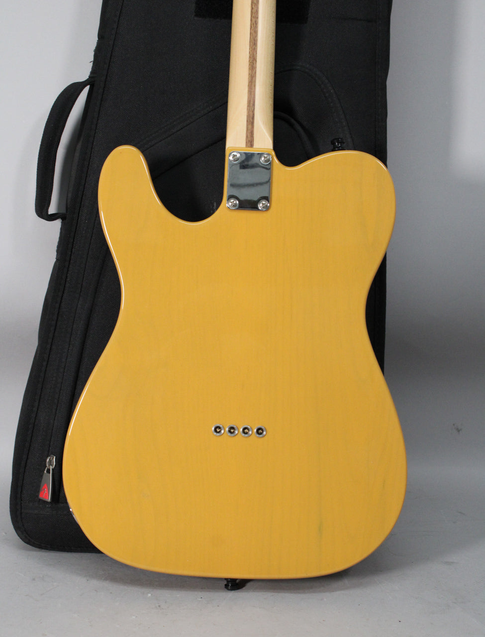 The back of a butterscotch blonde guitar with a visible wood grain, chrome neck plate, and four string ferrules.